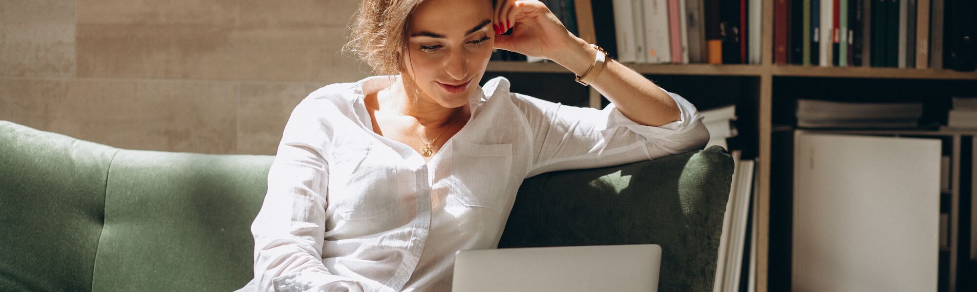 Professional woman in white shirt working on laptop in modern office with bookshelf