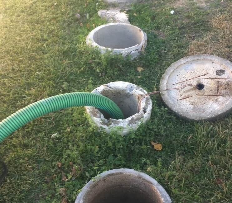 Septic system maintenance with green hose connected to concrete tank lids in grassy yard